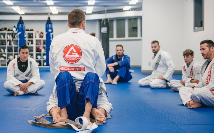Adult students gathered in a circle at the start of a Brazilian Jiu-Jitsu class